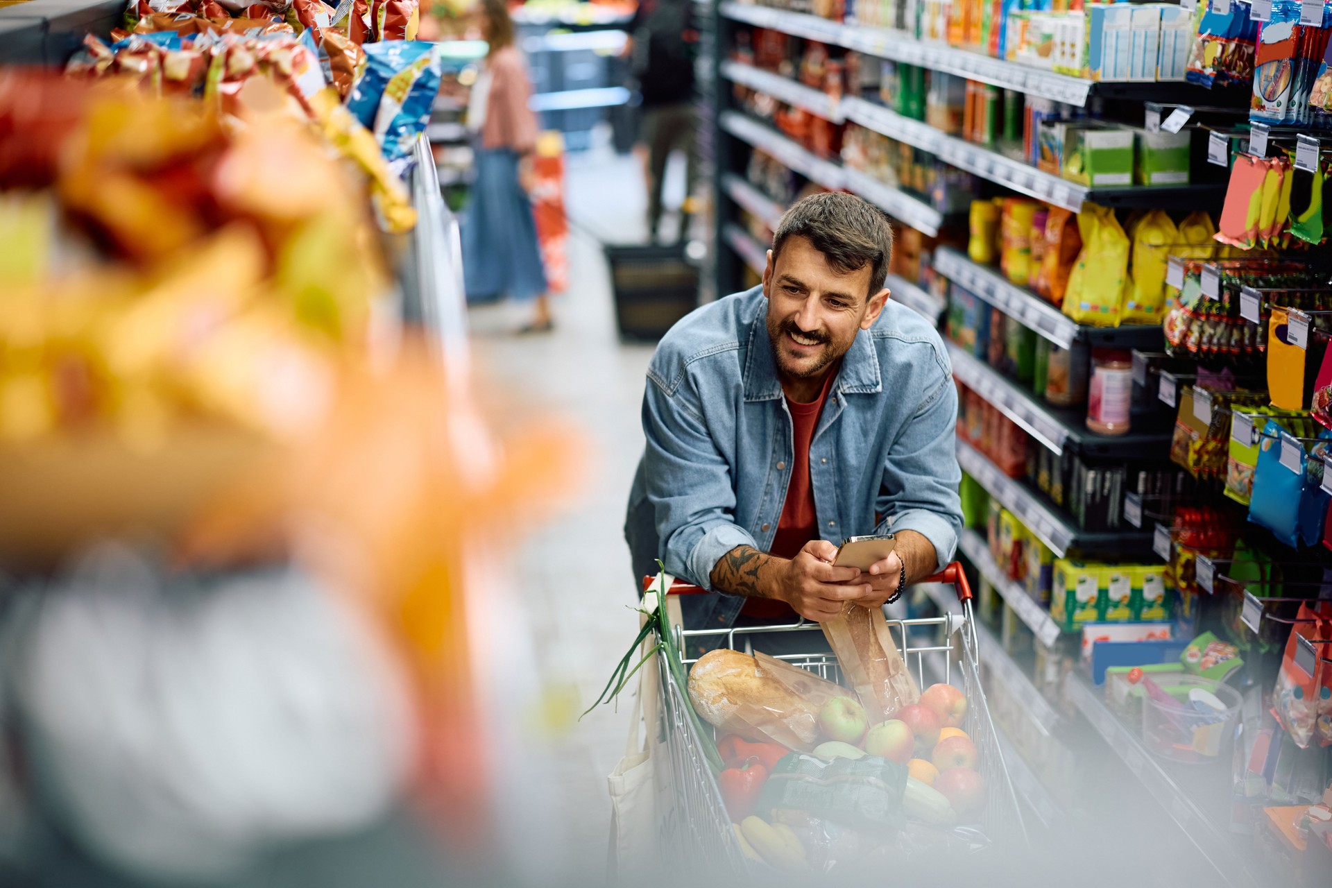 Happy man using mobile phone while buying groceries in supermarket.