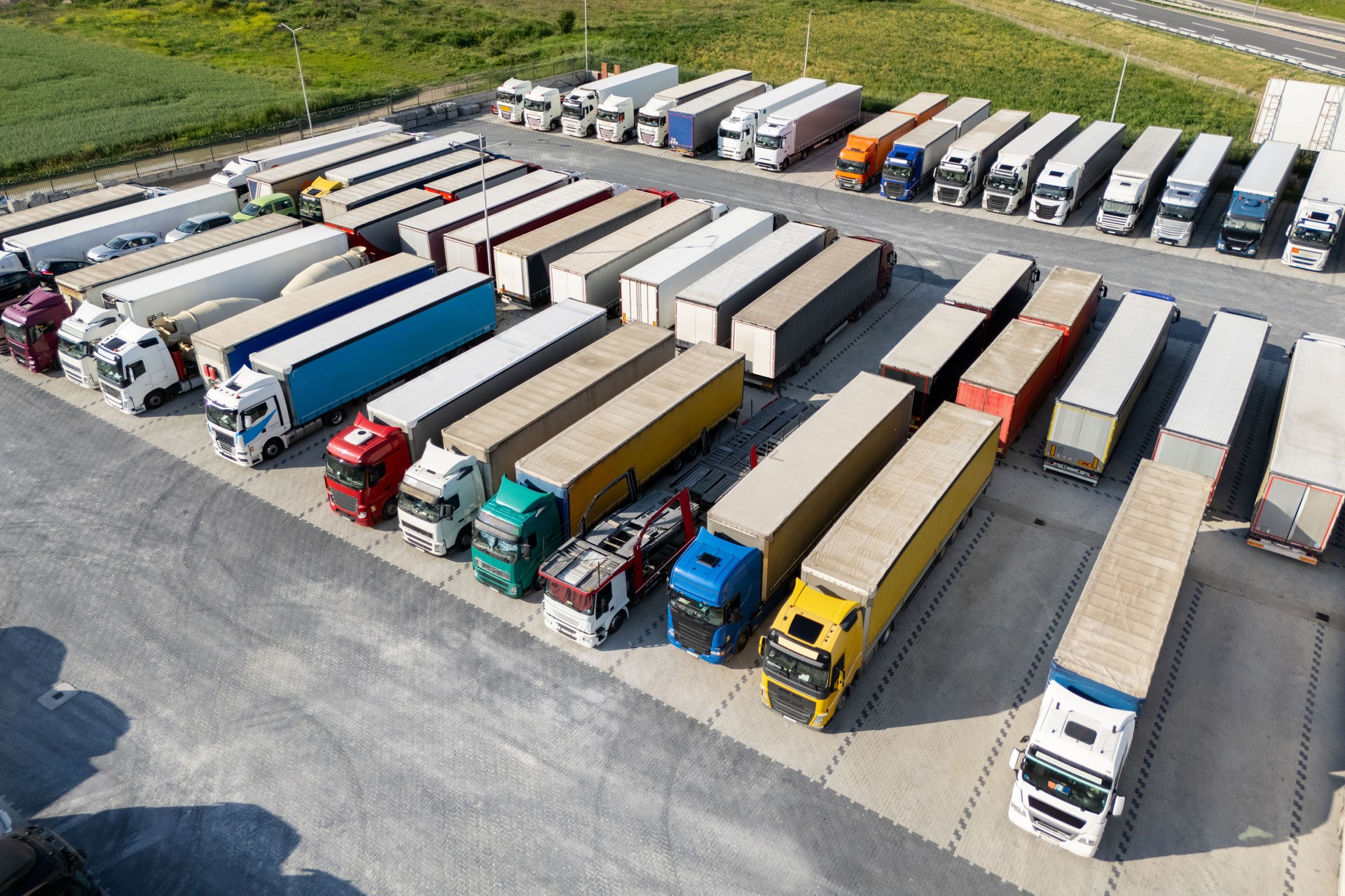 Aerial view of a large truck parking lot at a logistics hub, with multiple commercial semi trucks parked in organized rows.